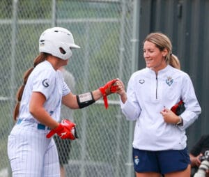 A softball athlete wearing white fist bumps a coach at first base